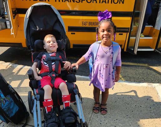Children in front of a school bus. One is in a wheelchair and the other is standing next to him..